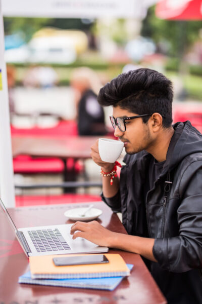 Indian Man using laptop while drinking a cup coffee street cafe